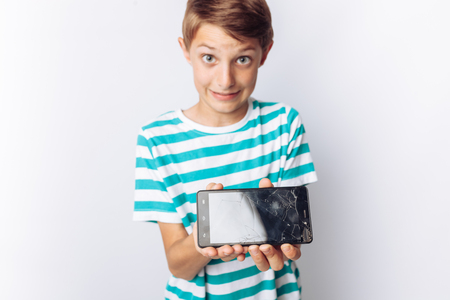Portrait of a beautiful and emotional boy, in whose hands a broken phone shows surprise, white background, blue t-shirt,の写真素材