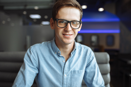 Portrait of a handsome young man, hipster posing with a serious look in glasses, sitting in a cafe,の写真素材