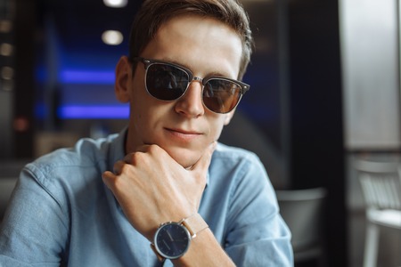Portrait of a handsome young man, hipster posing with a serious look in glasses, sitting in a cafe,の写真素材
