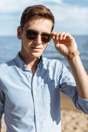 Beautiful stylish guy with glasses, posing on the beach, hipster posing in stylish clothes,の写真素材