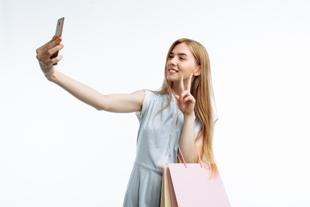 Young stylish girl, with gift bags, posing and taking a selfie on the phone with shopping, on a white background,の写真素材