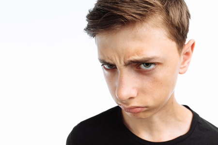 Portrait of a teenager, a guy showing emotions of sadness and resentment, in a black t-shirt, on a white background,の写真素材