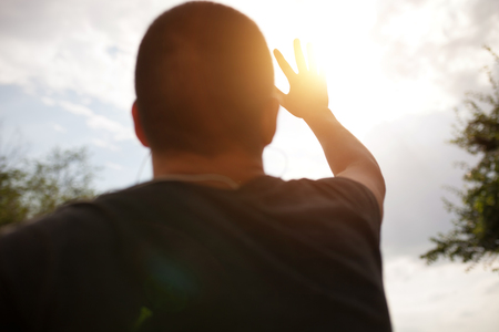 a hand reaches for the sky and covers the sun, the sun's rays make their way through the hand, close - upの写真素材