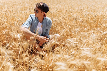 Portrait of a man in a wheat field, a guy with glasses and a capの写真素材
