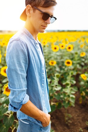 Portrait of a man in a cap and glasses, on the background of a field with sunflowers, travel with a touristの写真素材
