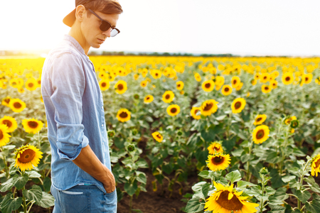 Portrait of a man in a cap and glasses, on the background of a field with sunflowers, travel with a touristの写真素材