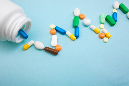 Multi-colored tablets and capsules in pulsation heartbeat white bottle for tablets, pharmaceutical medicine pills on blue background, analgesic against diseasesの写真素材