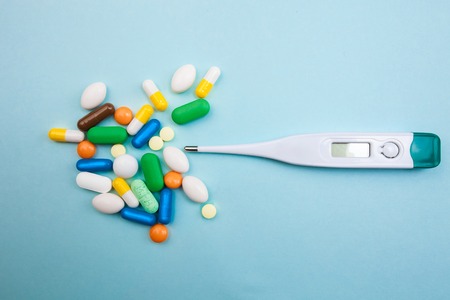 Multi-colored tablets and capsules, a thermometer and a tonometer on a blue background, concept of...