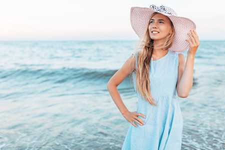 Beautiful portrait of a girl in a hat close-up, rest on the sea or ocean, a woman in a summer blue dressの写真素材
