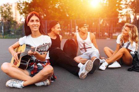 A group of friends having fun at sunset on the asphalt in a skate Park, playing guitar, good summer moodの写真素材