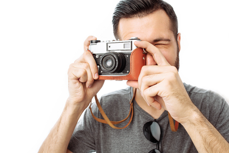 Portrait of a beautiful hipster guy in sunglasses, the photographer takes pictures with a camera while standing against white backgroundの写真素材