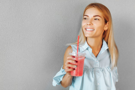Portrait of a young and beautiful girl student standing at the white wall with a cocktail in her handsの写真素材