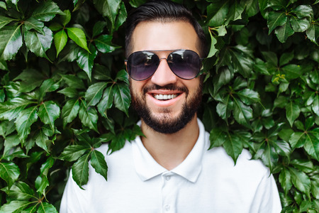 Stylish hipster in a white t-shirt and sunglasses, against a green leafy wallの写真素材