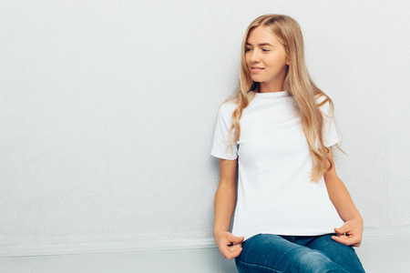 Young beautiful girl in white t-shirt sitting on floor on grey wall backgroundの写真素材