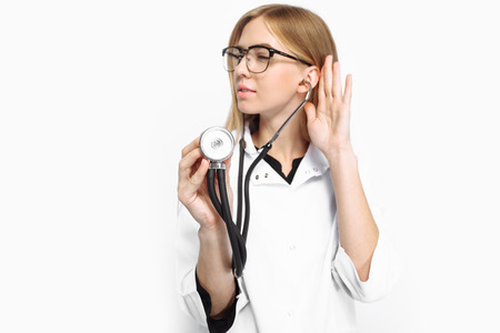 Young handsome intern doctor with glasses, using a stethoscope to listen to the patient's breath, isolated on a white background. Concept, medicine, healthの写真素材