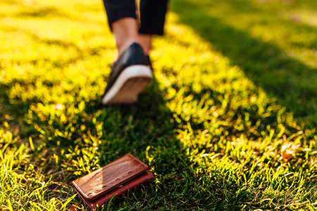 The girl lost a leather wallet with money on the street. Close-up of a purse and legs of a departing girlの写真素材
