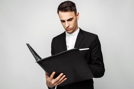 A successful man in a black suit with a folder in his hand working with documents on a gray background.の写真素材