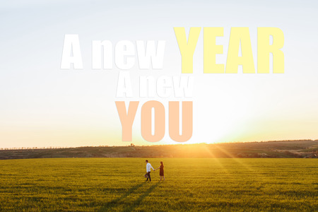 happy loving couple, at sunset, standing on a green field, against the sky, holding hands. Photos with text. New year new me. love conceptの写真素材