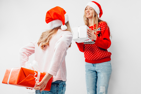 Mom and daughter celebrate the New Year, in Santa hats and Christmas sweaters, give each other Christmas presents, on a white background.の写真素材