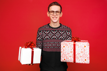 A man in glasses, with two gift boxes in his hands, on a red backgroundの写真素材