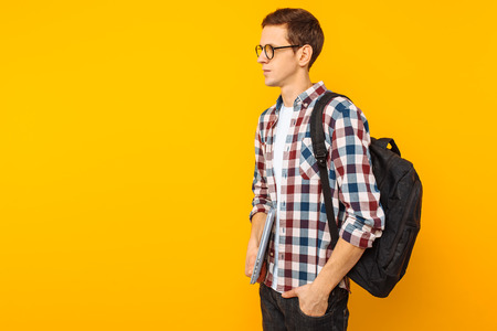 Happy guy with glasses, a student in a plaid shirt, with a closed laptop in hand, on a yellow backgroundの写真素材