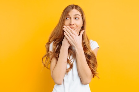 the girl covered her mouth with both hands, the woman shocked on a yellow background, the concept of...