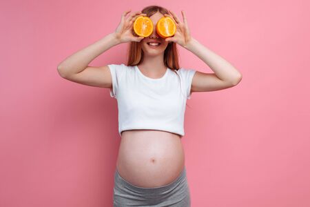 Beautiful pregnant woman with orange fruit on a pink background