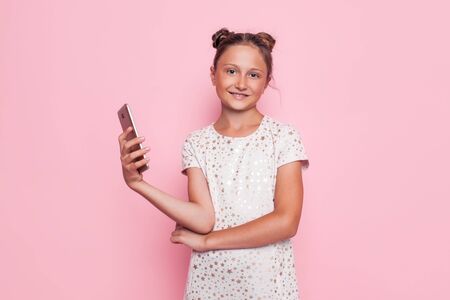 Portrait of a cute teenage girl, with a smartphone in hand, on a pink background