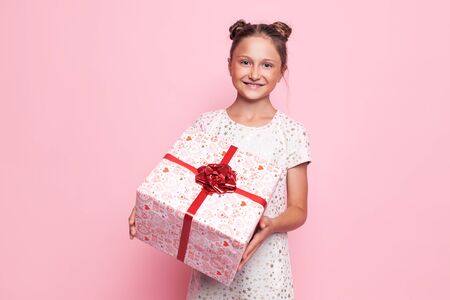 Portrait of a happy teenage girl with a gift box in her hands on a pink backgroundの写真素材