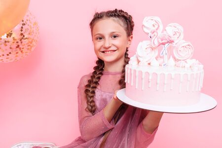 A teenage girl with balloons holds a cake in her hands, on a pink background. Birthday conceptの写真素材