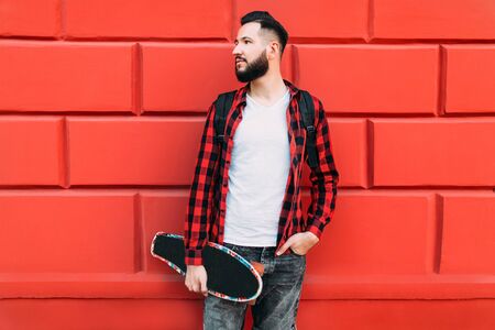 Stylish guy with a beard on a background of a brick empty wall with a skateboardの写真素材