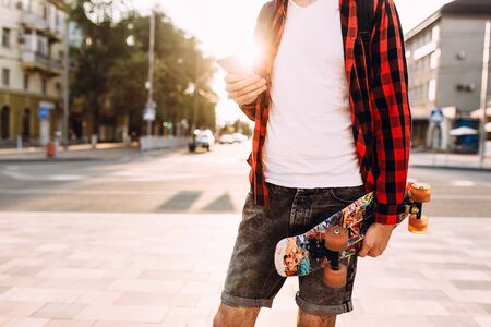 Stylish guy with a beard, walks around the city with a skateboard and a smartphone in his handsの写真素材