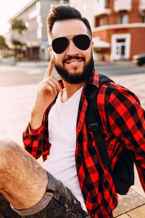 Stylish guy with a beard in wireless headphones is talking, sitting in the cityの写真素材