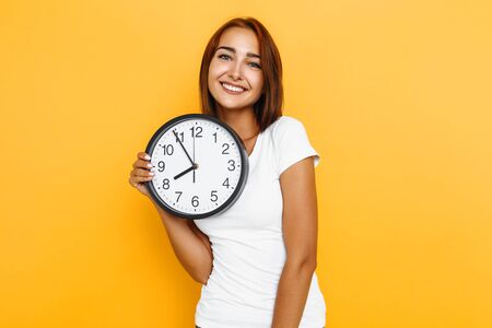 Young happy woman, in white t-shirt, with clock on yellow backgroundの写真素材