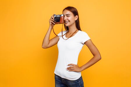 Young stylish girl photographer, woman taking photo with retro camera. Portrait on yellow background