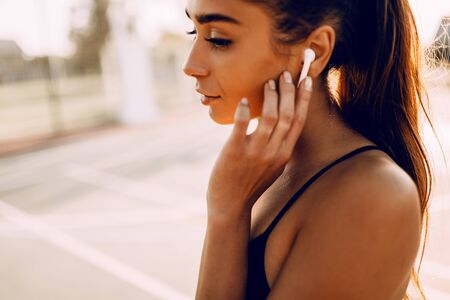 Image of sporty beautiful young girl wearing wireless headphones, listening to music during outdoor...