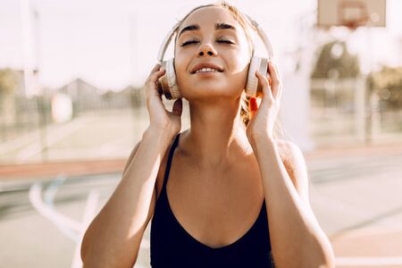 Happy athletic young woman, in sportswear, standing outdoors and listening to music with headphones, before trainingの写真素材