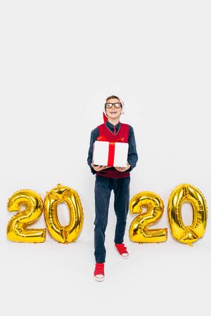 2020 New year A little boy in a Santa hat, a stylish child with a Christmas gift in his hands, on a white background with gold figures 2020. The Concept Of A New Yearの写真素材