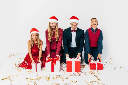Young happy Christmas family with kids wearing Santa hats while sitting opening Christmas gifts, on white background. New Year, Christmas, holidayの写真素材