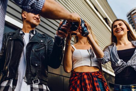 A group of positive friends, girls and guys walk around the city together at the black wall, have fun and drink drinksの写真素材