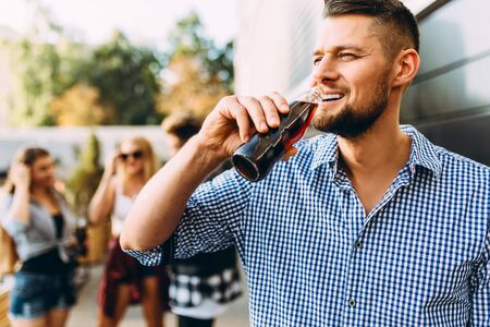 A group of young friends, girls and guys walking together in the city, having fun and drinking drinks, in the foreground stylish attractive guyの写真素材