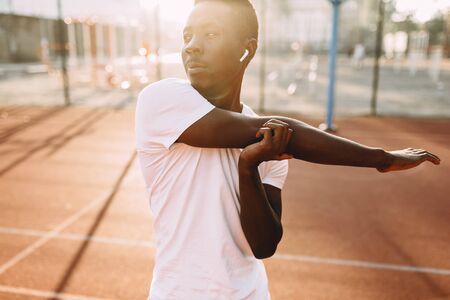 Athletic African-American doing stretching exercises, preparing for a morning workout at the stadium...
