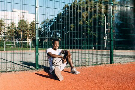 Strong young African American resting after training sitting in the stadium leaning on the fence,...