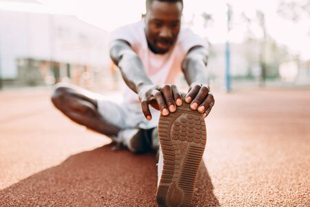 Athletic African-American doing stretching exercises, preparing for a morning workout at the stadium at dawnの写真素材