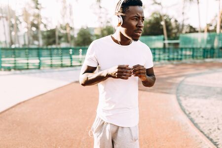 Sporty young African American listening to music in headphones, morning jog at the stadium in the...