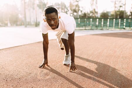 Portrait of a young African-American athlete standing at the start of the running track in the stadium, preparing for the raceの写真素材