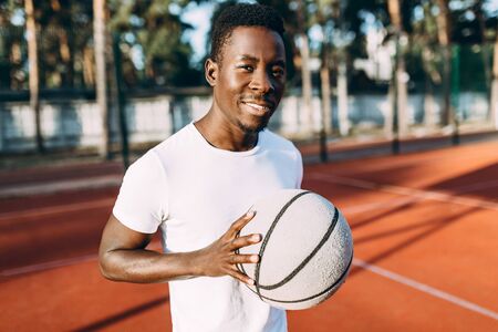 Sporty young African American standing on the court at dawn with a ball, basketball player, morning exercise, active lifestyleの写真素材