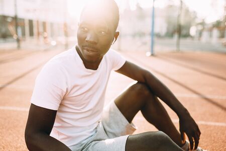 Sporty young African American posing sitting on court at dawn, morning exerciseの写真素材
