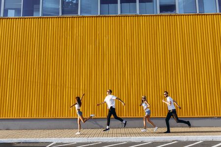 happy group of young people have fun while running and jumping in the city, against the yellow wall...