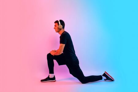 Young fitness man with headphones doing stretching exercises on background with red and blue neon...